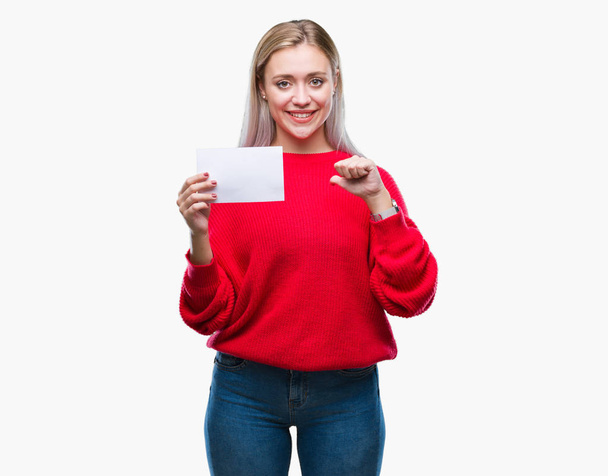 Young blonde woman holding blank paper card over isolated background with surprise face pointing finger to himself - Fotoğraf, Görsel