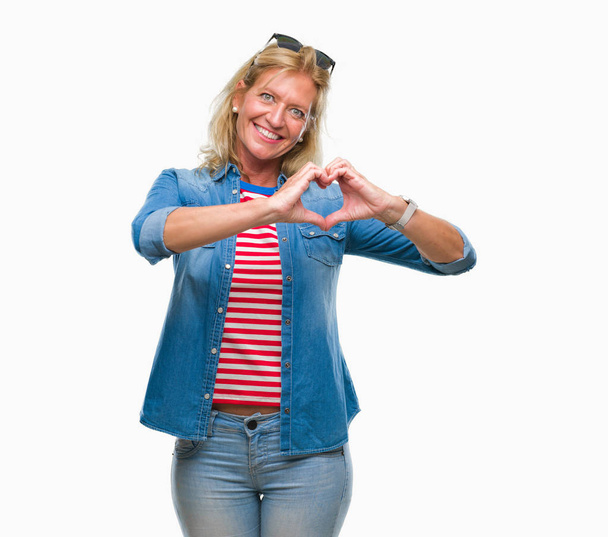 Μέσης ηλικίας ξανθιά γυναίκα πέρα από το απομονωμένο υπόβαθρο χαμογελώντας στην αγάπη που δείχνει το σύμβολο της καρδιάς εμφανίζεται και το σχήμα με τα χέρια. Ρομαντική έννοια. - Φωτογραφία, εικόνα
