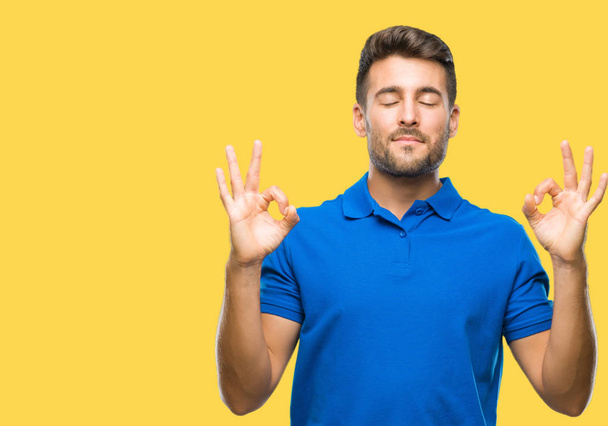 Young handsome man over isolated background relax and smiling with eyes closed doing meditation gesture with fingers. Yoga concept. - Fotoğraf, Görsel