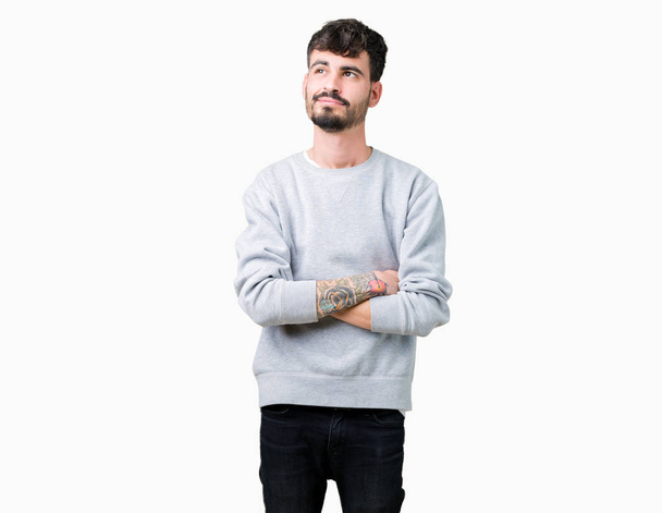 Jonge knappe man dragen sweatshirt over geïsoleerde achtergrond glimlachend uitziende kant en staren weg denken. - Foto, afbeelding