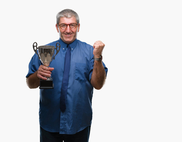 Guapo sénior exitoso hombre sosteniendo trofeo sobre fondo aislado gritando orgulloso y celebrando la victoria y el éxito muy emocionado, animando emoción
 - Foto, Imagen