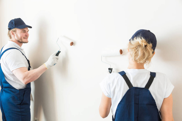deux ouvriers peignent professionnellement les murs de la pièce. personnes en uniforme, en salopette et une casquette avec un rouleau et une brosse, rénovation de l'appartement, design intérieur, teinte. isolé
 - Photo, image