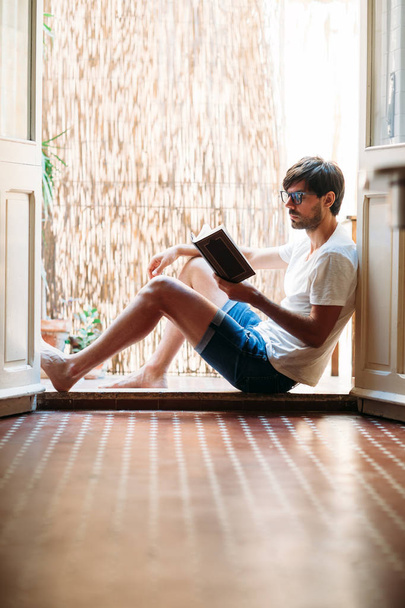 Young man reading book sitting on balcony at home. Relax and weekend concept - Foto, Imagen