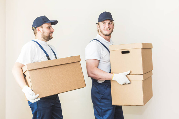 Delivery man loading cardboard boxes for moving to an apartment. professional worker of transportation, male loaders in overalls - Foto, afbeelding
