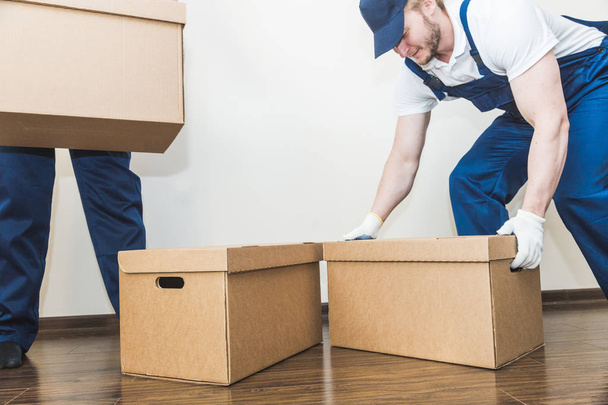 Delivery man loading cardboard boxes for moving to an apartment. professional worker of transportation, male loaders in overalls - Foto, Imagen