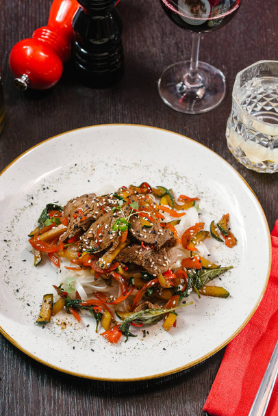 primer plano vista de copa de vino y plato asiático con carne, fideos y verduras
 - Foto, imagen