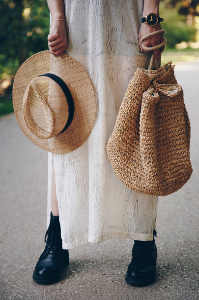 Close up of a stylish woman holding a straw hat and bag in her hands on a sunny day outside - Foto, Imagem