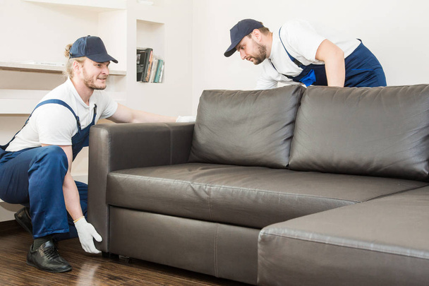 Entrega hombre mover muebles llevar sofá para mudarse a un apartamento. trabajador profesional del transporte, cargadores masculinos en overol
 - Foto, imagen