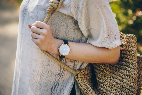 Крупним планом стильна жінка в літній сукні і тримає солом'яну сумку під час носіння стильного наручного годинника
 - Фото, зображення