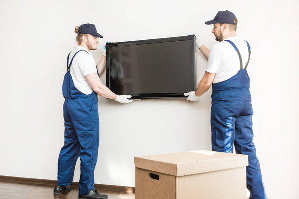 Delivery manremove the TV from the wall for moving to an apartment. professional worker of transportation, male loaders in overalls - Photo, Image
