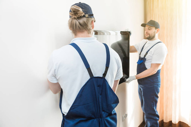 Delivery manremove the TV from the wall for moving to an apartment. professional worker of transportation, male loaders in overalls - Foto, Imagen