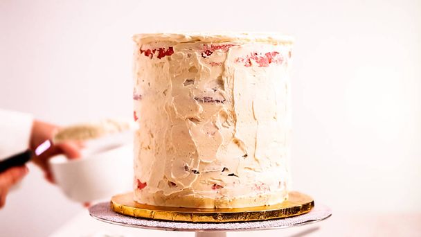 Baker berijpen roze en paarse taart met een witte botterroom suikerglazuur. - Foto, afbeelding