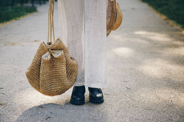 Detalhe de estilo de rua de uma mulher em um vestido de verão usando botas de couro de tornozelo e segurando um saco de palha
 - Foto, Imagem