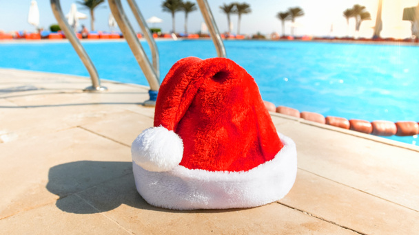 Parlak güneşli bir günde yüzme havuzuna karşı kırmızı Noel Baba şapka Closeup görüntü - Fotoğraf, Görsel