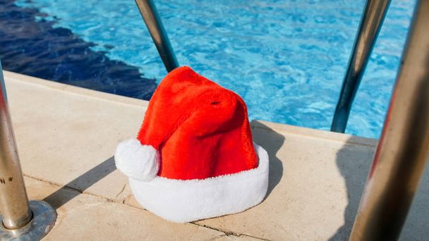 Immagine di Babbo Natale ha lasciato il suo cappello piscina all'aperto. Concetto di viaggio e turismo a Natale, Capodanno e vacanze invernali
. - Foto, immagini