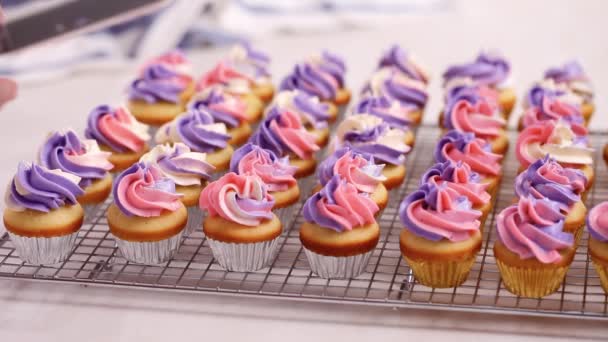 Csővezeték rózsaszín és lila vajkrém fagyosan, a kis vanília cupcakes. - Felvétel, videó