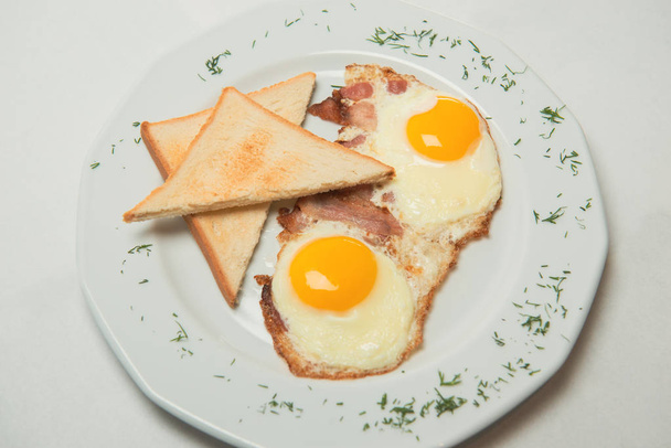 Chutný sázená vejce na bílé plotně s topinkami a slaniny zdobené zelení. Výživná snídaně.  - Fotografie, Obrázek
