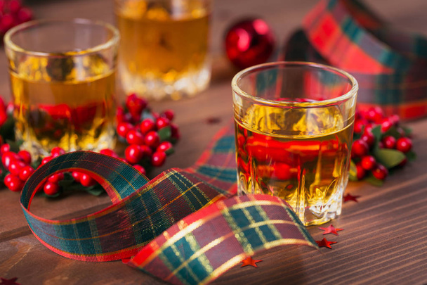 Whiskey, brandy or liquor shot and Christmas decorations on wooden background. Seasonal holidays concept. - 写真・画像