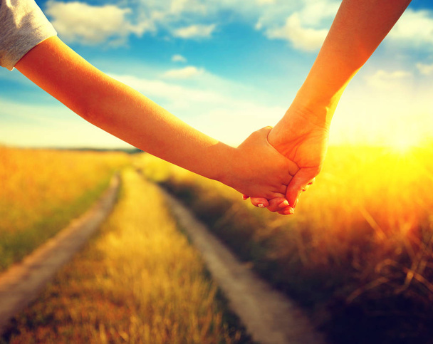 Hands of holding each other in field on road and sun - Photo, Image
