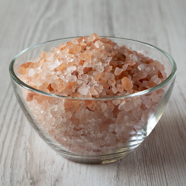 Himalayan sea salt in a glass bowl on white wooden surface, side view. Closeup. - Foto, imagen