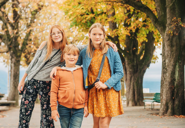 Retrato al aire libre de 3 niños divertidos, dos niñas y un niño posando juntos en el parque de otoño
 - Foto, Imagen
