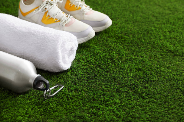 Bottle of water, sneakers, towel and space for text on artificial grass. Fitness equipment - Foto, Imagen