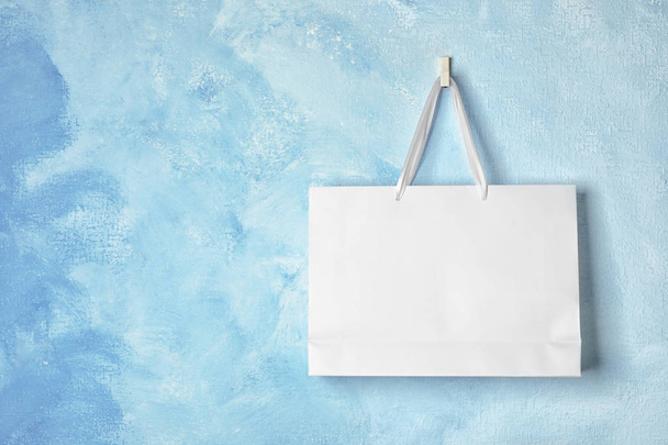 Paper shopping bag with handles hanging on color wall. Mock up for design - 写真・画像