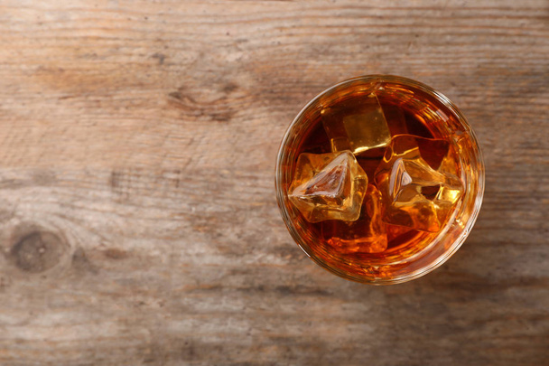 Golden whiskey in glass with ice cubes on wooden table, top view. Space for text - Valokuva, kuva