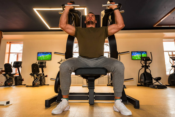 Young muscular man does lower chest exercises with machine in modern gym - Fotoğraf, Görsel