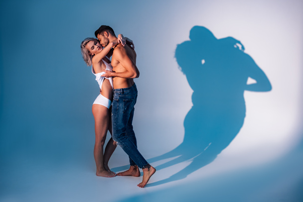 shirtless man hugging and kissing woman with shadows on dark blue background - Foto, afbeelding