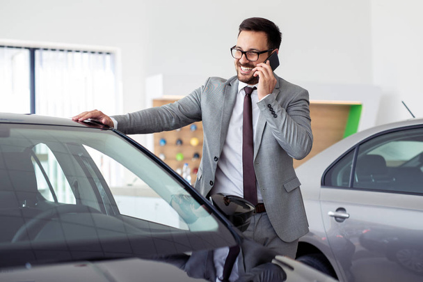 Businessman having a phone call at the car showroom  - Fotó, kép