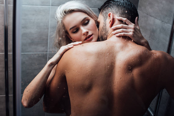 affectionate heterosexual couple hugging and kissing while taking shower together - Fotó, kép