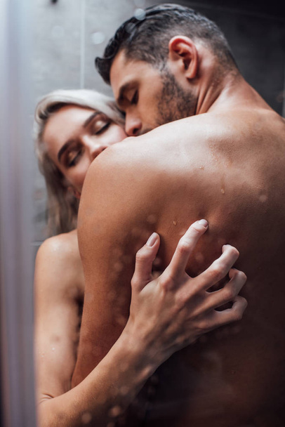 selective focus of passionate naked heterosexual couple hugging and kissing while taking shower together - Фото, зображення