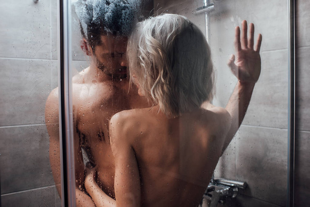 nude heterosexual couple looking at each other, embracing and taking shower together - Fotó, kép