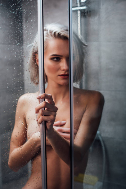 naked sensual woman holding shower door, looking away and posing in bathroom - Фото, зображення