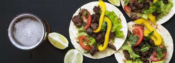 Ízletes taco a marhahús és a zöldségek, a sör és a lime fekete felületen, felülnézete. Mexikói konyha. Lapos feküdt, top view, felülről. - Fotó, kép