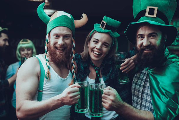 Saint Patrick's Day Party. Group of Friends is Celebrating. People is Drinking a Green Beer. Friends is Young Men and Women. Happy Men Toast with Each Other. People Wearing a Green Hats. Pub Interior. - Foto, Imagen