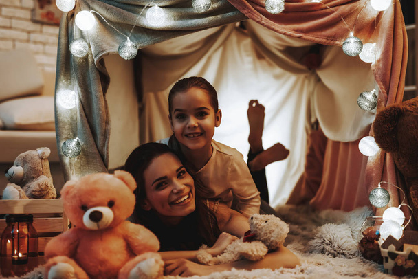 Mother and Daughter Lying on Terry Carpet. Persons is Lying Under the Fake Tent. Daughter is Hugging Her Mother. Persons is Happy and Smiling. Evening Time. People in Home Interior. - Foto, Imagem