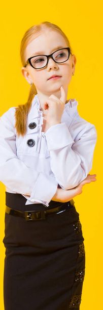 Girl with red hair on a yellow background. A charming girl in transparent glasses put a finger to her chin. - Photo, Image
