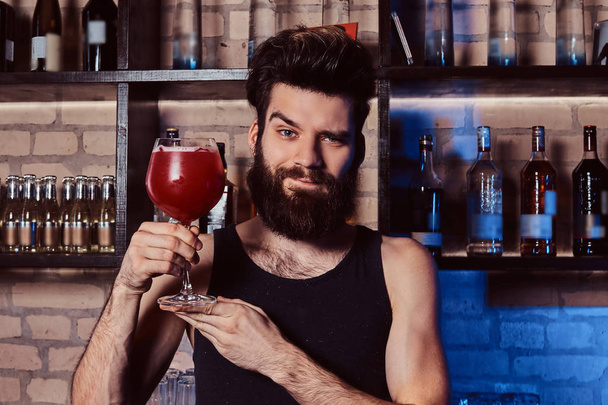Hezký vousatý barman drží sklenici s Aperol spritz koktejl při pózuje pro kameru za barovým pultem - Fotografie, Obrázek