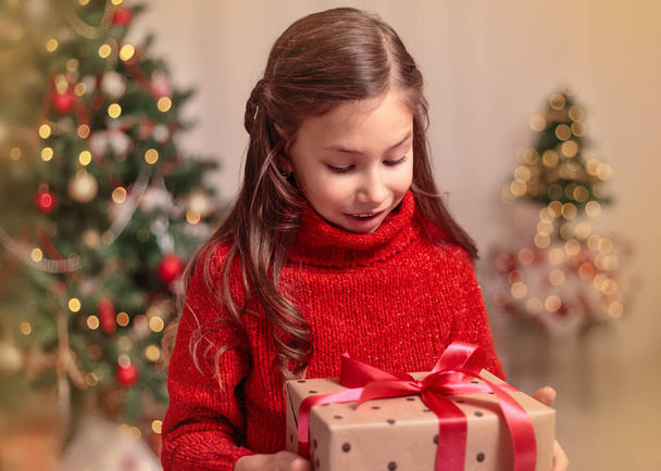 Cute little child girl with present gift box near Christmas tree at home. - Photo, Image