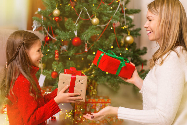 Cheerful mom and her cute daughter girl exchanging gifts. Merry Christmas and Happy Holidays. - Фото, зображення