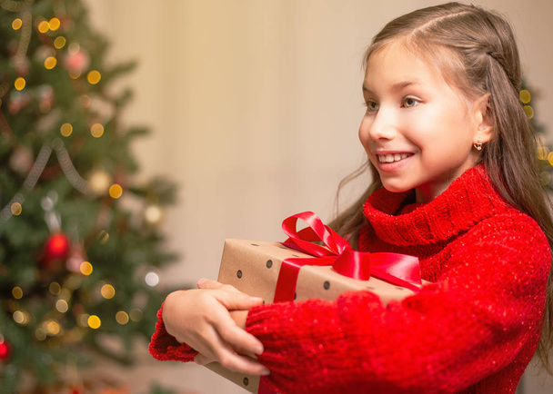 Schattig klein kind meisje met huidige doos van de gift in de buurt van de kerstboom thuis. - Foto, afbeelding