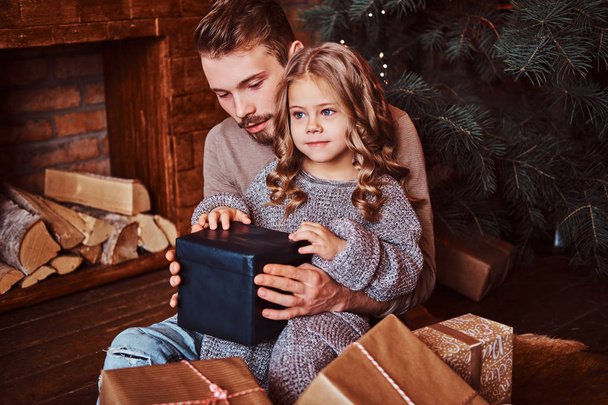 Αγάπη, οικογένεια, πατρότητα, Χριστούγεννα. Ευτυχία ο πατέρας και η κόρη του χαριτωμένο μικρό άνοιγμα δώρα ενώ κάθεται στο πάτωμα - Φωτογραφία, εικόνα