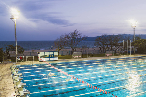 Varna, Bulgaria, November 2018. Swimming complex Primorsky on the Black Sea coast. Outdoor sport swimming pool lit by powerful spotlights on a dark autumn evening sky background - Foto, immagini