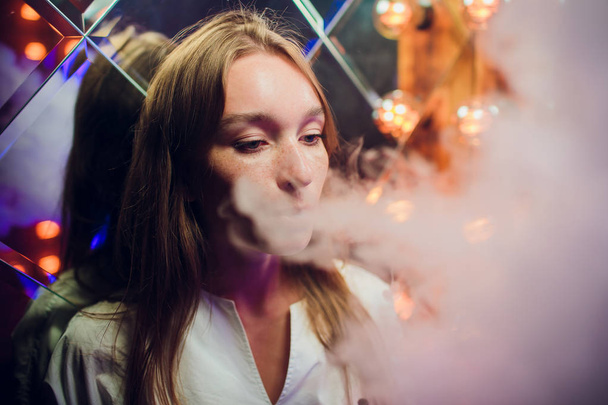 young woman smoking electronic cigarette against background of mirrors - Foto, afbeelding