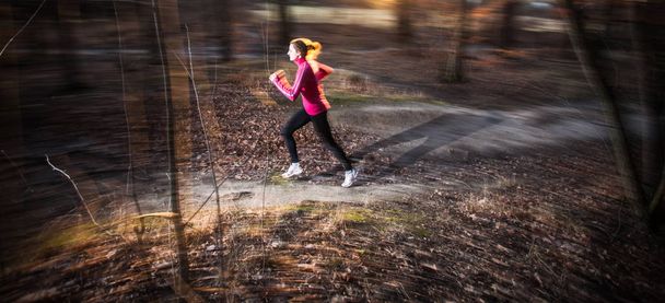 Young woman running outdoors in a city park on a cold fall/winter day (motion blurred image) - Foto, afbeelding