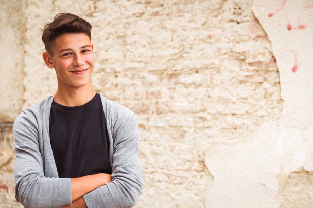 Portrait of the young man who is standing outdoor near the old house wall and smiling - Fotoğraf, Görsel