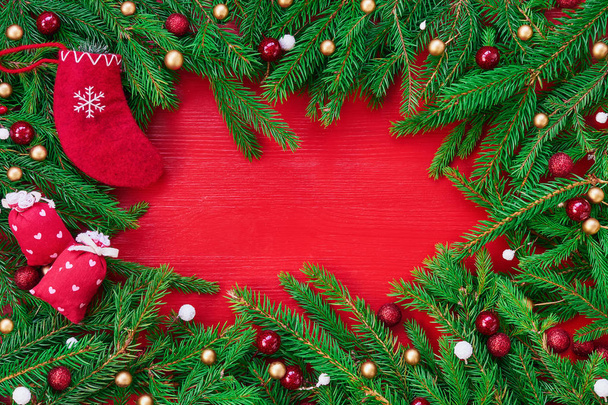 Red Christmas background. Christmas tree branches with decoration and red Christmas socks on red wooden background. Copy space, top view - Foto, Bild