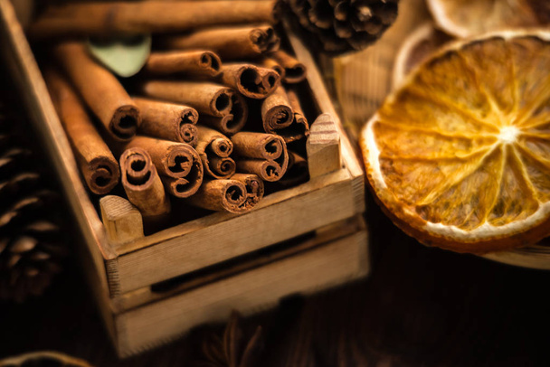 Christmas bakery and New Year concept. Holiday background with dried lemon citrus slices and set of cinnamon sticks. Cosy winter holiday baking spices set on dark wooden background.  - Foto, afbeelding